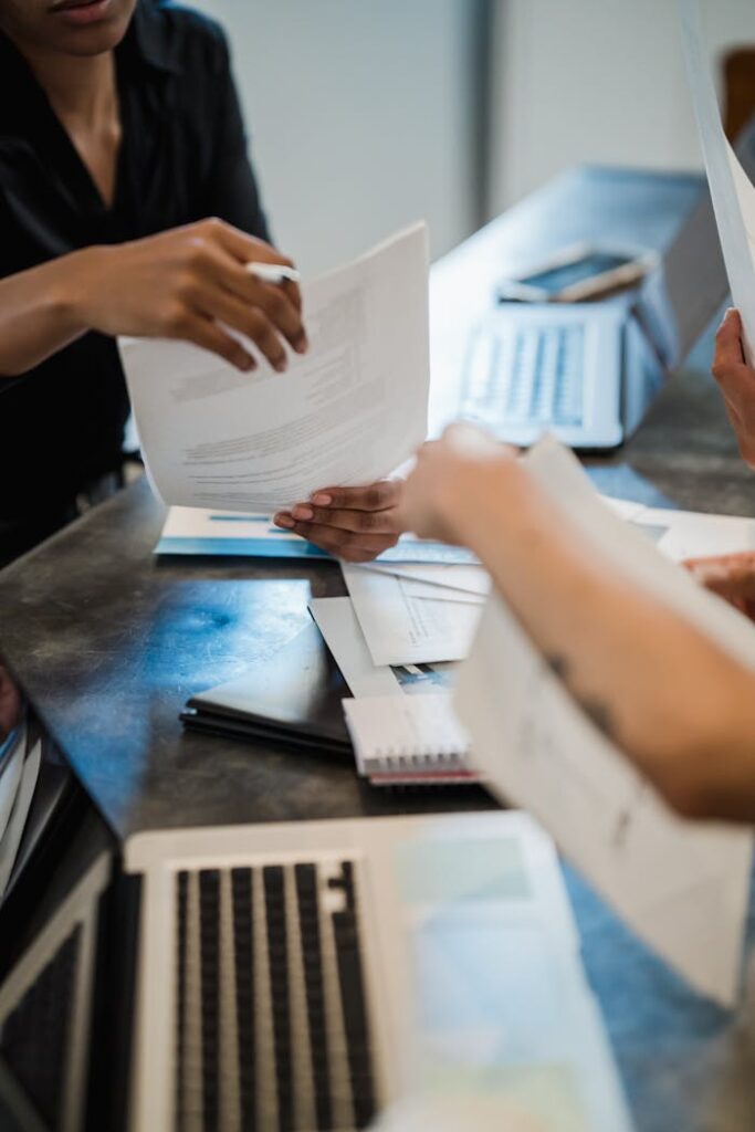 Hands exchanging documents in an office meeting setting with laptops.